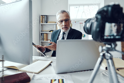 Senior man in elegant business suit using modern technologies while making social media video