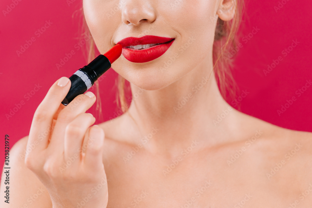 cropped view of naked beautiful woman with red lips applying lipstick isolated on crimson cropped view of naked beautiful woman with red lips applying lipstick isolated on crimson