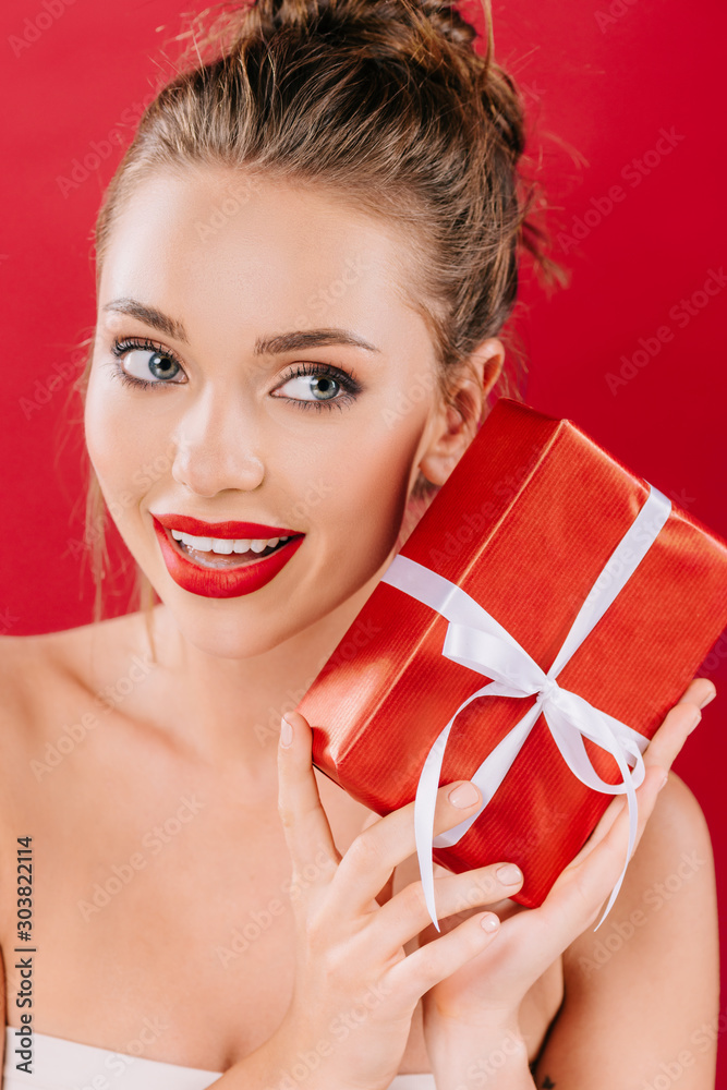 beautiful woman with red lips holding gift box isolated on red beautiful woman with red lips holding gift box isolated on red