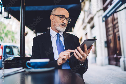 Elderly bearded businessman sitting and working on tablet