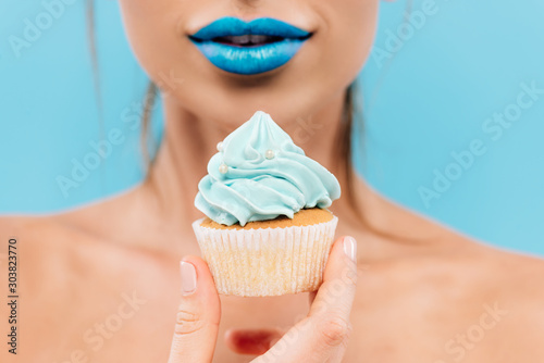 selective focus of naked beautiful woman with blue lips and cupcake isolated on blue