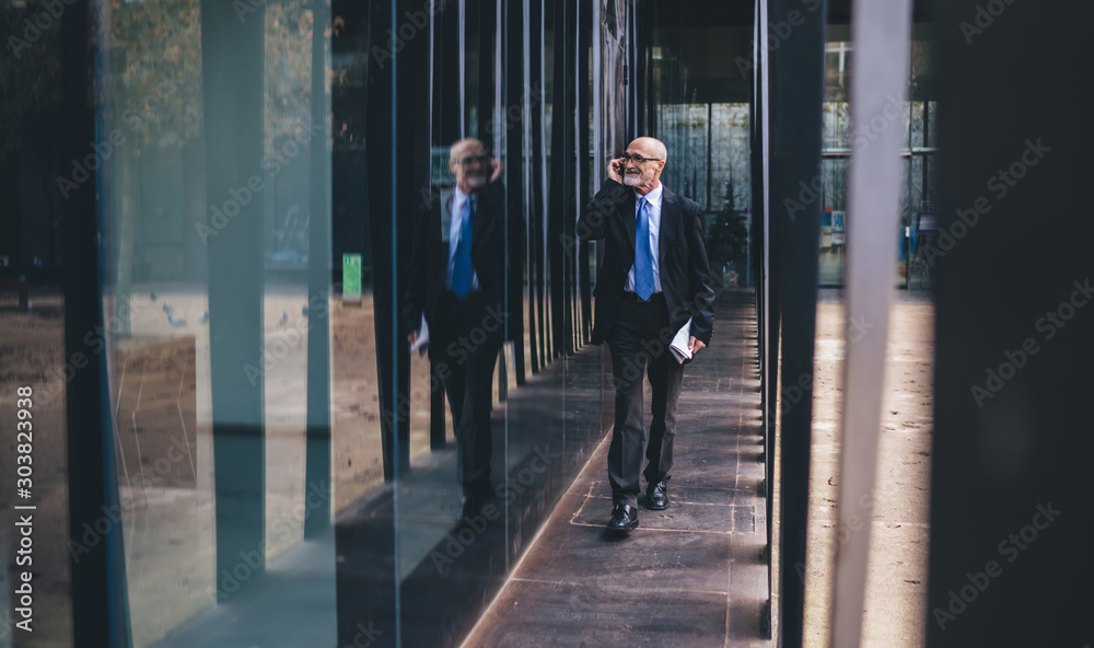Cheerful old businessman in suit having phone call on street Cheerful old businessman in suit having phone call on street