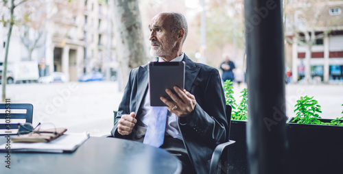 Thoughtful businessman in street cafe with tablet
