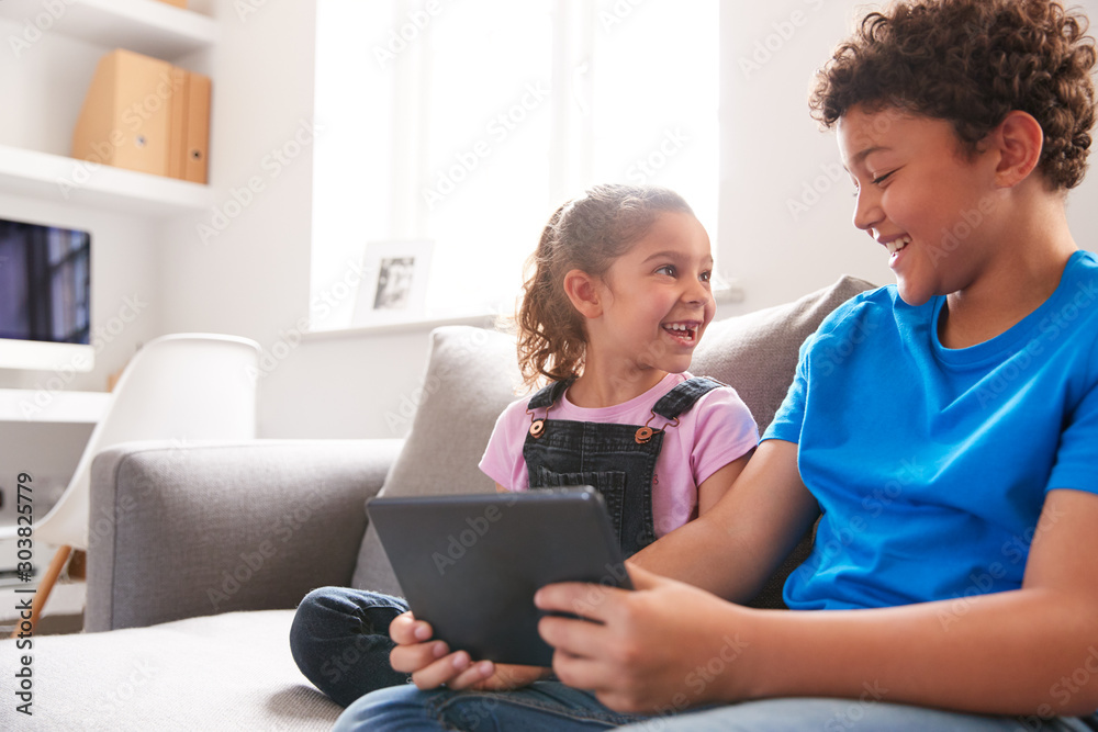 Brother And Sister Sitting In Lounge At Home Watching Movie On Digital Tablet Together Brother And Sister Sitting In Lounge At Home Watching Movie On Digital Tablet Together