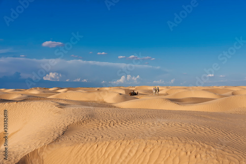 the sands and dunes of the Sahara desert  with camels and people sitting on camels
