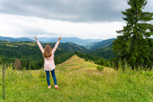 Happy woman standing on green hill and looking at mountains