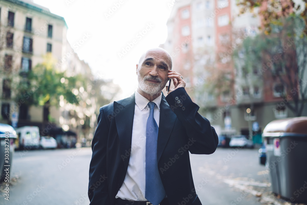 Thoughtful senior businessman in suit having phone call while walking on street Thoughtful senior businessman in suit having phone call while walking on street