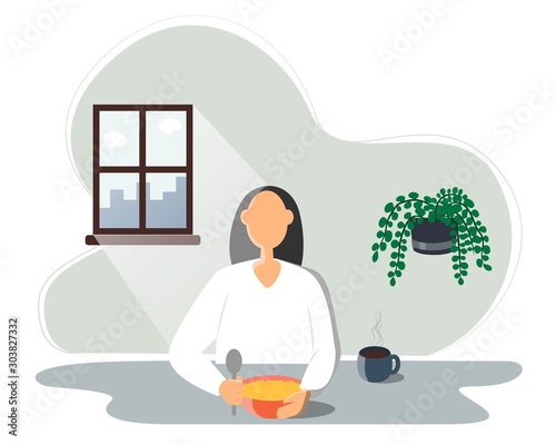 woman eating food, young woman sitting at the table and having breakfast. In a bowl of porridge, next to a Cup of hot tea or coffee. The sun shines brightly through the window. Healthy food before the