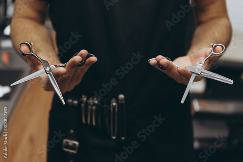 Professional hairdresser prepares for a haircut, checks his tool, examines scissors holding them in his hands, focus on scissors. concept for barbershops, beauty salons and hairdressers photo