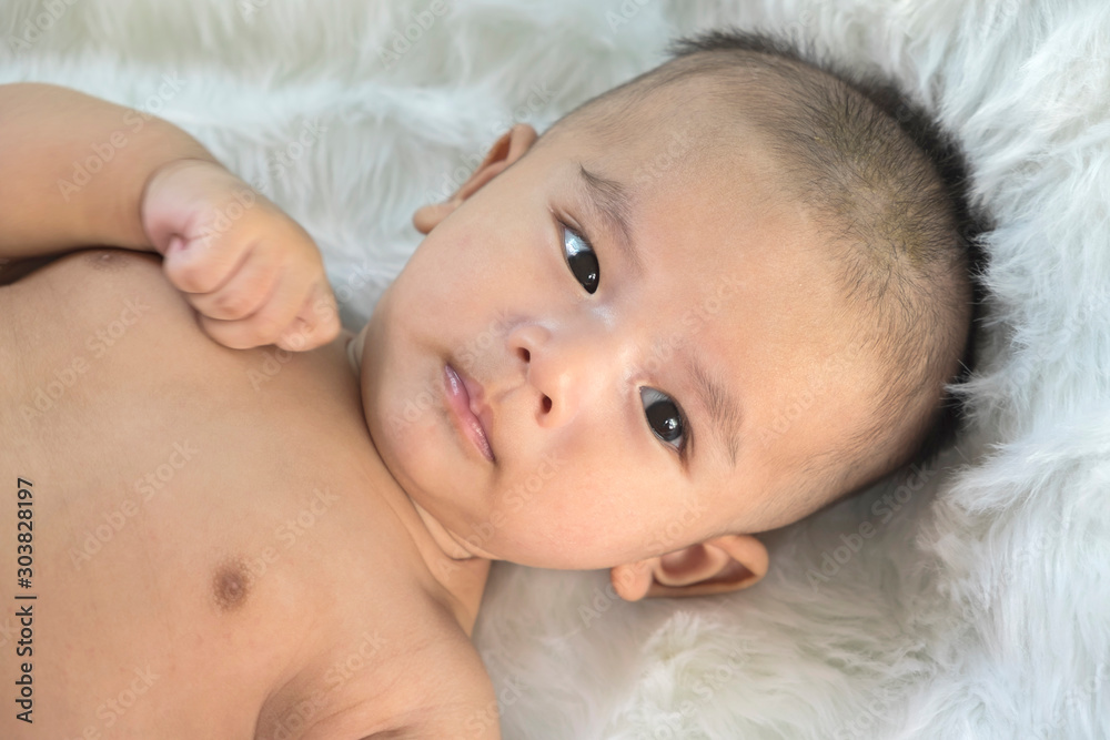 Peaceful newborn baby lying on a bed smiling on white sheets Peaceful newborn baby lying on a bed smiling on white sheets