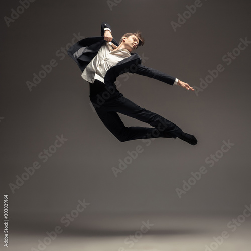 Man in casual office style clothes jumping and dancing isolated on grey background. Art, motion, action, flexibility, inspiration concept. Flexible caucasian ballet dancer, weightless jumps.
