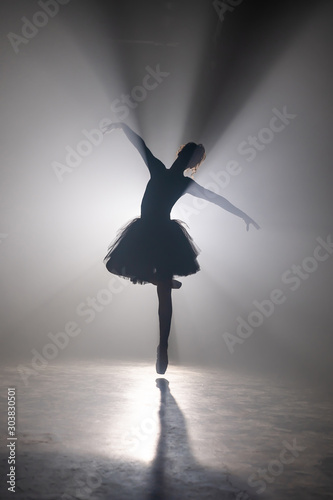 Professional ballerina dancing ballet in spotlights smoke on big stage. Beautiful young girl wearing black tutu dress on floodlights background. Black and white.