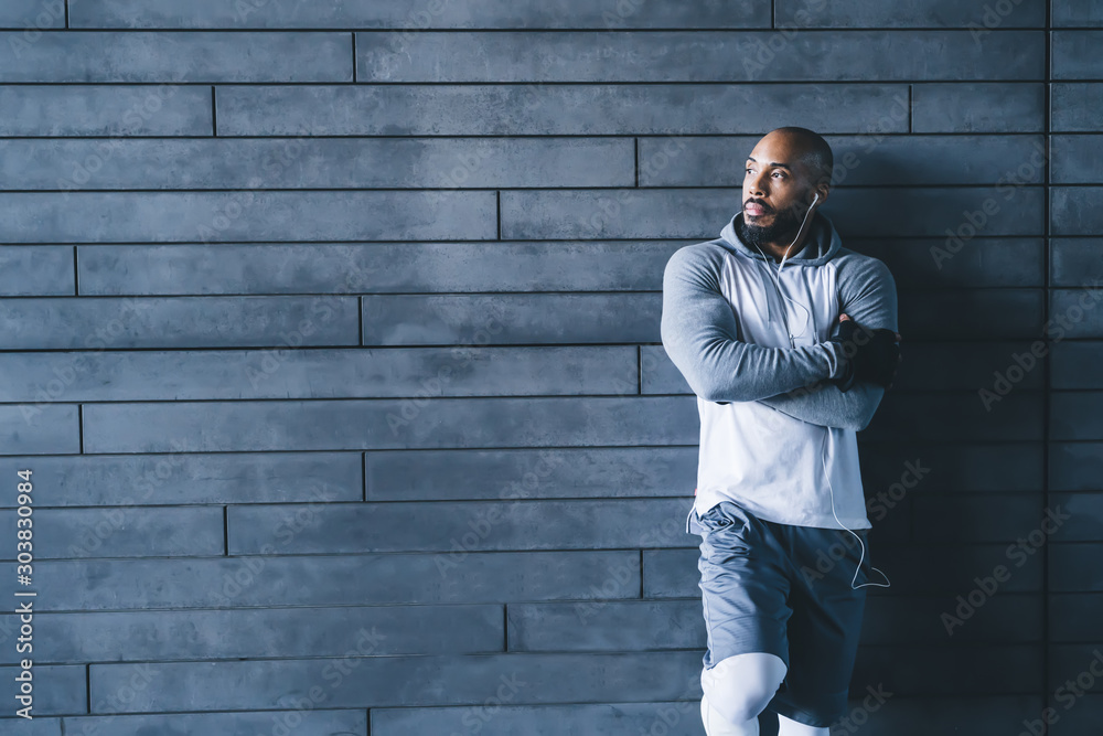 Muscular African American sportsman leaning leg on wall and crossing arms Muscular African American sportsman leaning leg on wall and crossing arms