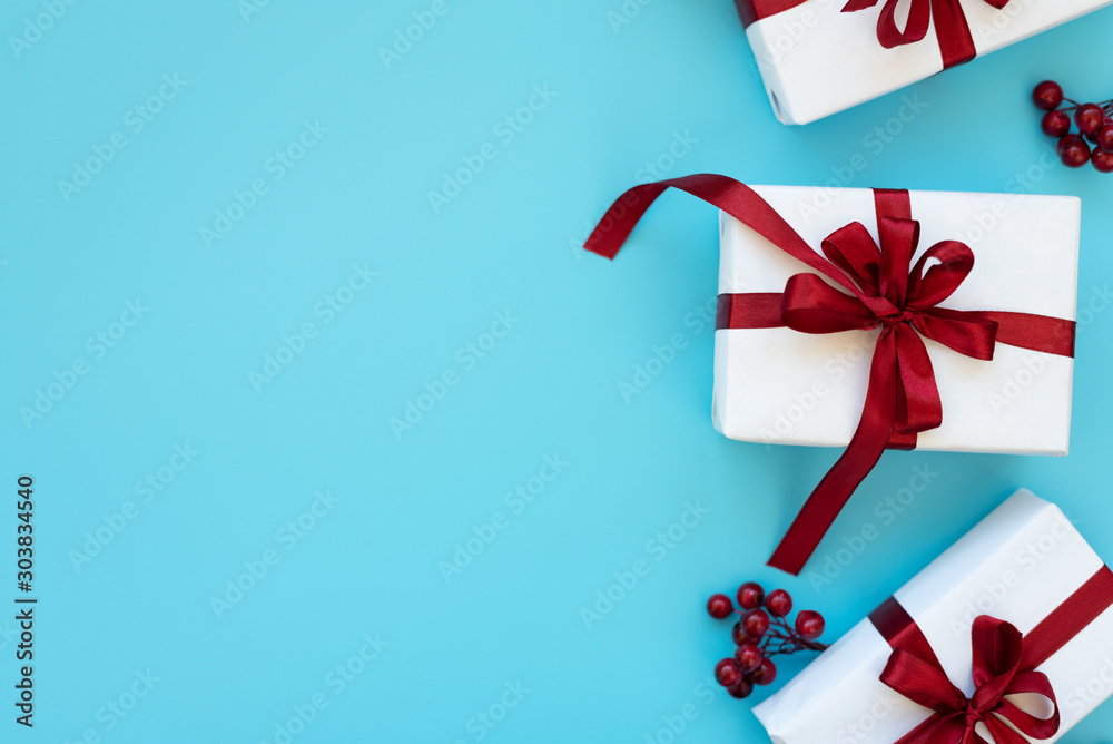 Gift boxes wrapped white paper and red ribbon decorated berries on blue background. Top view. Flat lay. Christmas and New Year holidays concept Gift boxes wrapped white paper and red ribbon decorated berries on blue background. Top view. Flat lay. Christmas and New Year holidays concept