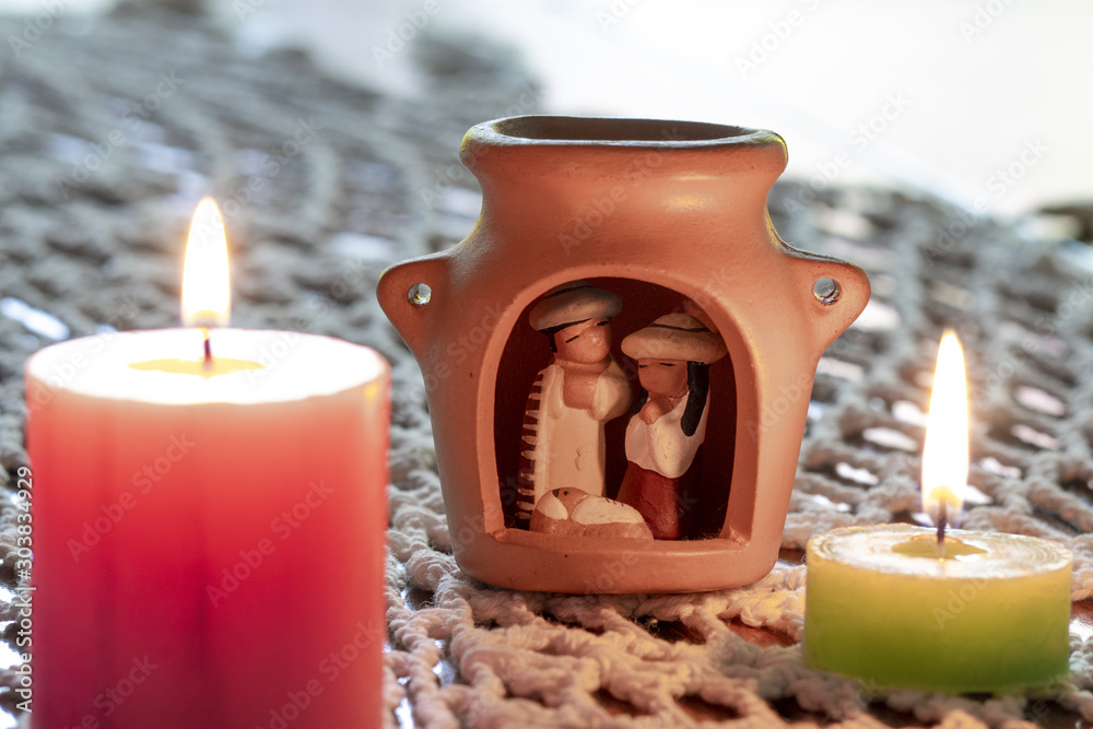 Φωτογραφία Velas decorativas de color rosa y verde con llamas encendidas sobre una alfombra tejida a crochet blanco junto a un pesebre de origen latinoamericano