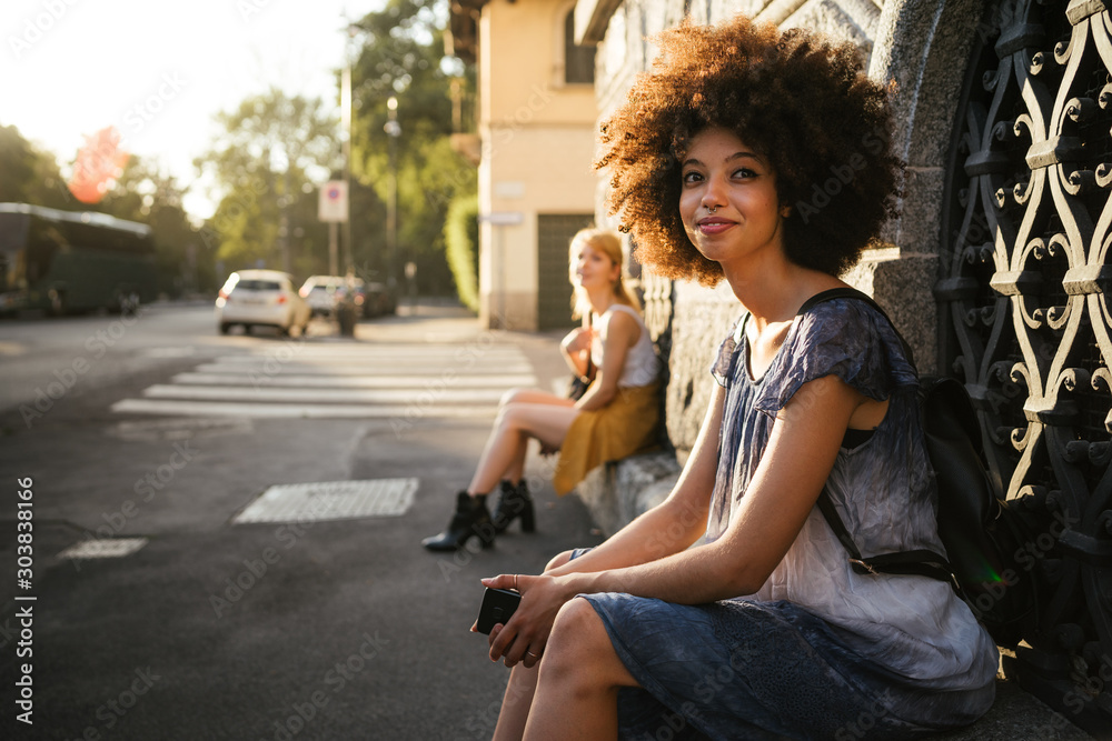 Φωτογραφία Young woman with afro hair is resting on a window sill on the sidewalk of a city