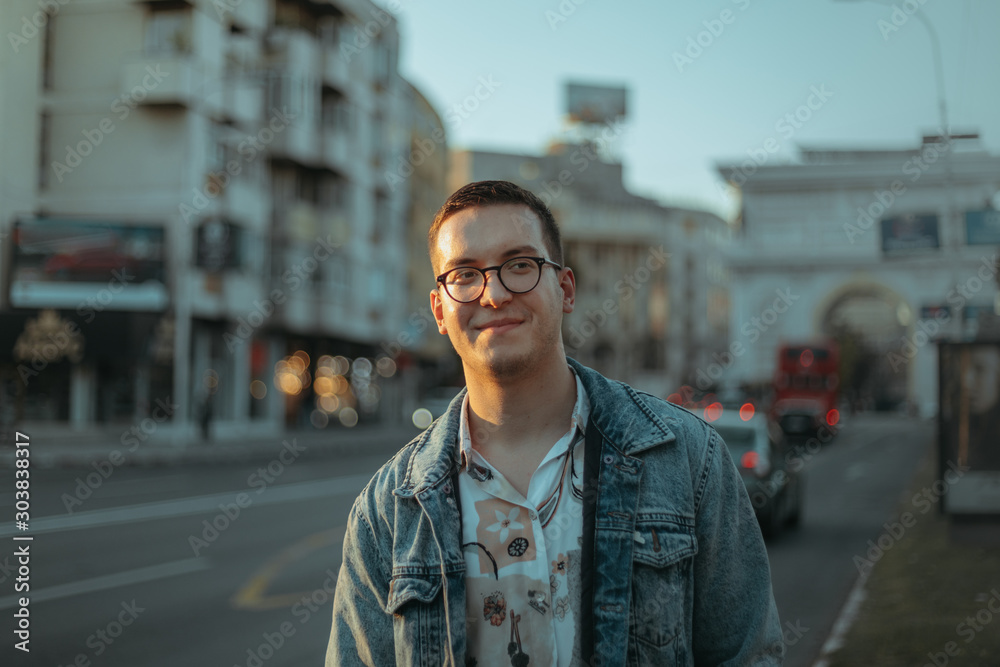 Young fashionable man walking on a boulevard in the city at sunset