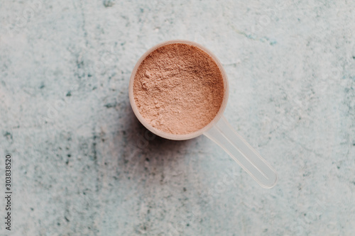 Scoop or spoon of whey protein with visible texture. Chocolate flavor. Concrete background