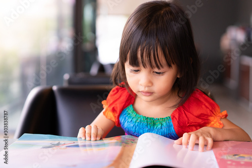 Adorable asian little girl is sitting and reading storybook on the sofa with concentrate happy moment, concept of activity for kid education.