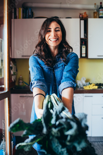 Young beautiful woman indoor kitchen at home showing a bunch of kale photo