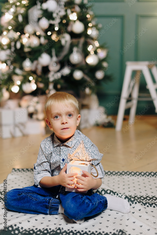 little beautiful boy on the background of a decorated Christmas tree with lights little beautiful boy on the background of a decorated Christmas tree with lights