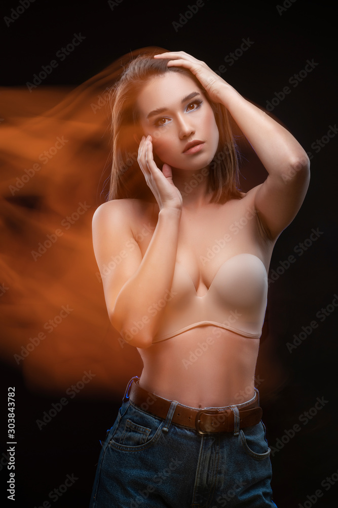 Beautiful mixed race Asian girl with big breasts, wearing a bra and jeans, moves and dances in long and multiple exposure. Advertising, commercial and artistic design.