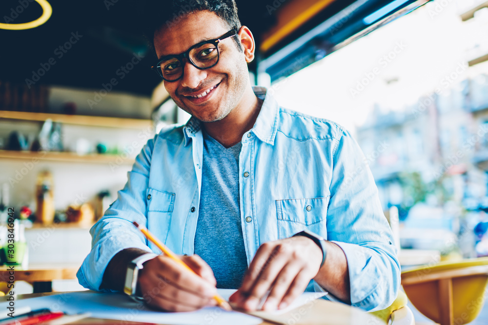 Φωτογραφία Half length portrait of handsome smiling male designer in stylish eyeglasses creating new sketches on paper