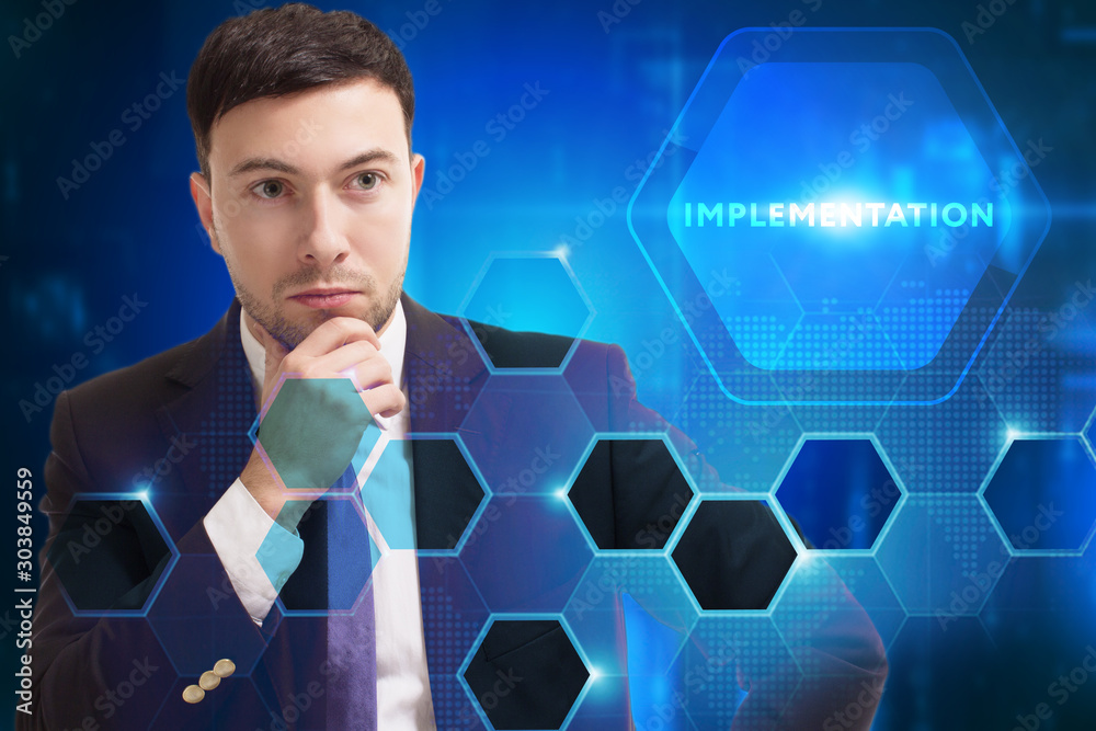 Business, Technology, Internet and network concept. Young businessman working on a virtual screen of the future and sees the inscription: Implementation Business, Technology, Internet and network concept. Young businessman working on a virtual screen of the future and sees the inscription: Implementation