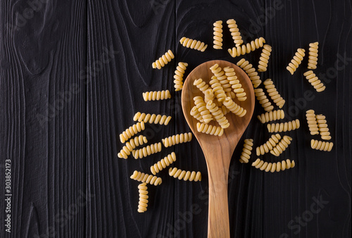 Top view of fusilli pasta on black wooden table with spoon photo