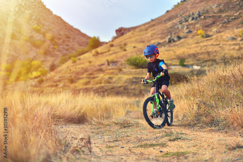 Happy kid boy of 7 years having fun in autumn park with a bicycle on beautiful fall day. Active child wearing bike helmet