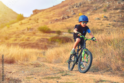 Happy kid boy of 7 years having fun in autumn park with a bicycle on beautiful fall day. Active child wearing bike helmet