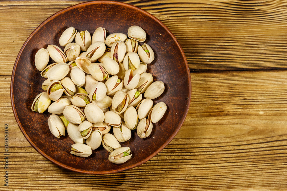 Pistachio nuts in ceramic plate on a wooden table. Top view Pistachio nuts in ceramic plate on a wooden table. Top view