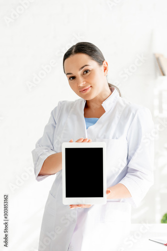 attractive dermatologist holding digital tablet and looking at camera in clinic