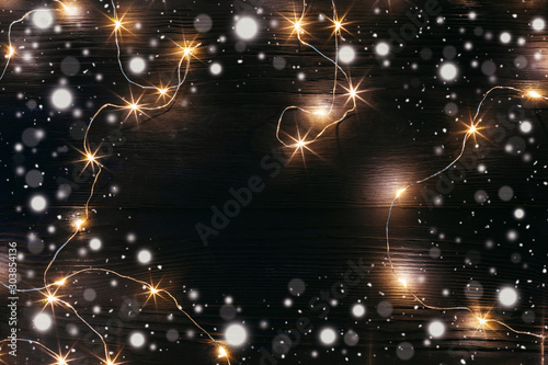 Christmas and New Year holydays composition. Lighted garland and a snow on dark wooden background. Flat lay, top view. Copy space.