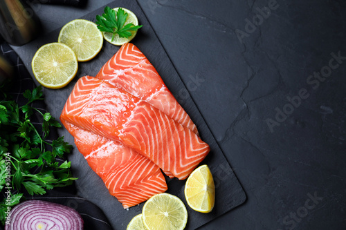 Flat lay composition with fresh raw salmon and products on black table, space for text. Fish delicacy photo