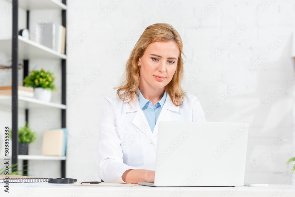attractive nutritionist sitting at table and using laptop in clinic attractive nutritionist sitting at table and using laptop in clinic