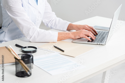 cropped view of nutritionist sitting at table and using laptop in clinic