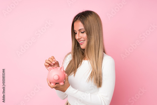 Young blonde woman over isolated pink background holding a big piggybank