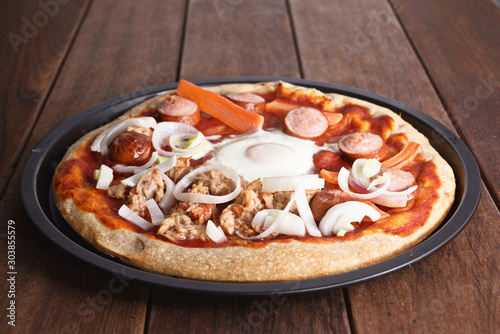 pizzza with egg, onion, tuna fish, carrot and frankfurter in a backing tin, on a wooden table, freshly baked photo