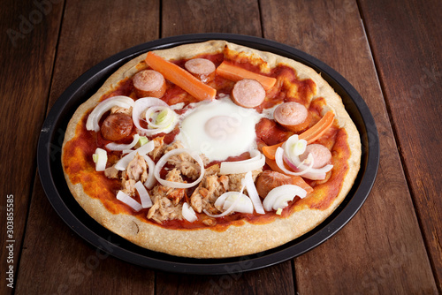 pizzza with egg, onion, tuna fish, carrot and frankfurter in a backing tin, on a wooden table, freshly baked photo