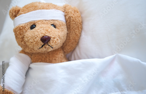 Teddy bear lying sick in bed With a headband and a cloth covered