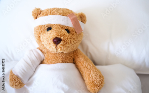 Teddy bear lying sick in bed With a headband and a cloth covered