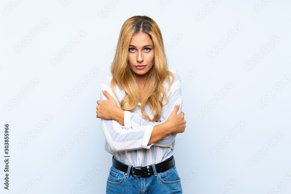 Young blonde woman over isolated blue background freezing Young blonde woman over isolated blue background freezing