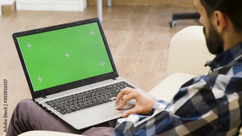Man on the sofa looking at green screen laptop
