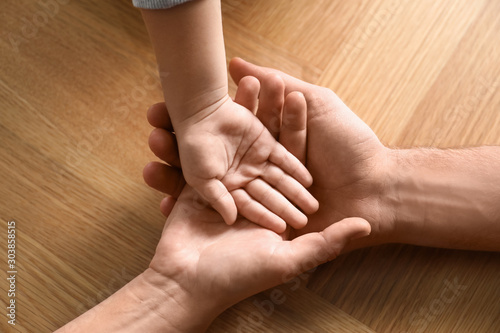 Happy family holding hands on wooden background, closeup