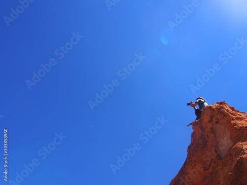 A man sitting on a rock under a bright blue sky while holding a camera, Laguna Misteriosa, Journey from San Pedro de Atacama in Chile to Uyuni in Bolivia
