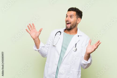 Young doctor man over isolated green wall with surprise facial expression