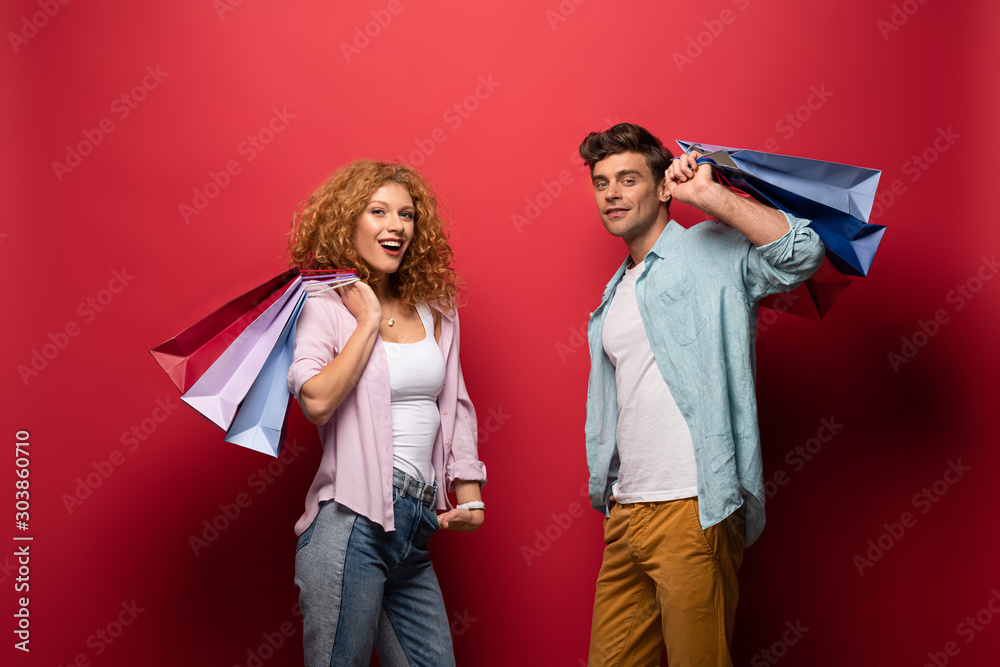 Εκτύπωση καμβά cheerful couple holding shopping bags, isolated on red