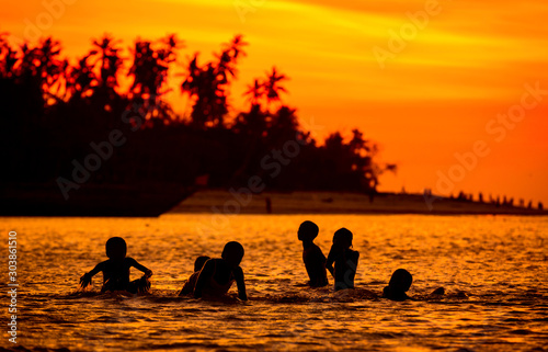 Silhouettes of children playing in the water at sunset