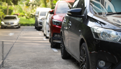 Closeup of front side of black car with other cars parking in outdoor parking area beside the street in sunny day. 